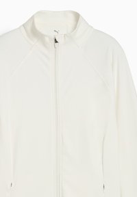 Veste zippée blanche en tissu doux et extensible, à col haut et manches raglan. Présente un logo discret au niveau du col et des poches latérales.