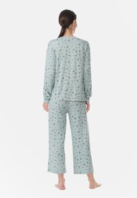 Vaaleansininen pyjamakokonaisuus, jossa on pitkähihaisena paita ja leveälahkeiset housut, joissa on kukkakuosi. Materiaali näyttää pehmeältä ja mukavalta.