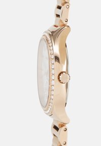Reloj de oro rosa con una caja redonda y pulida, adornada con cristales en el bisel. Pulsera de eslabones metálicos con una textura suave.