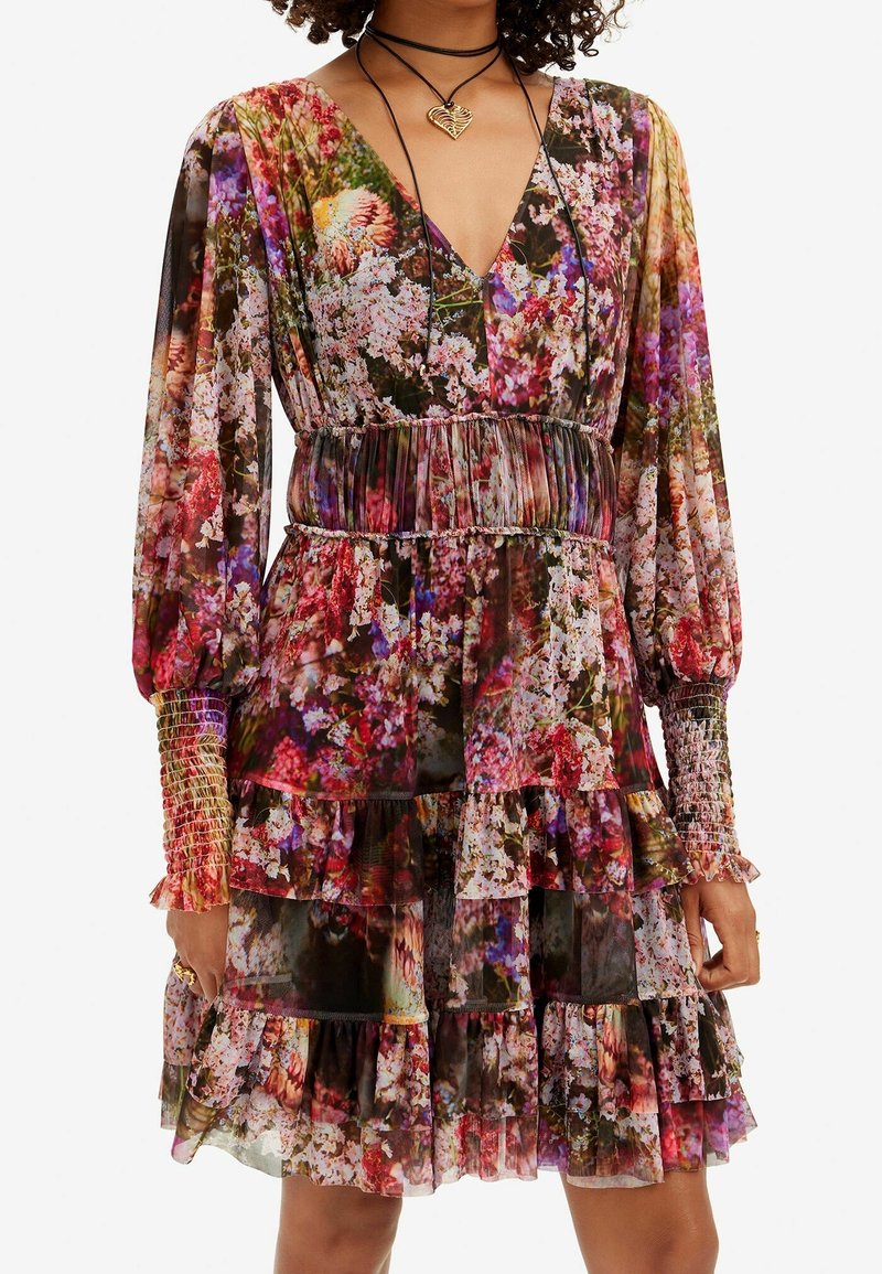 Robe longue à manches longues en voile transparent à motif floral, avec col en V, taille smockée et volants à étages. Présente des manches texturées dans une palette de couleurs pastelles.