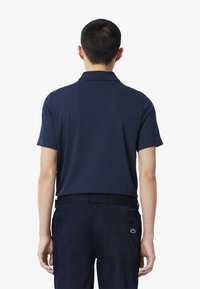 Marinblå polo t-shirt i bomull med korta ärmar och klassisk krage. Ytterligare detalj inkluderar en logotyp på vänster bakre sida.