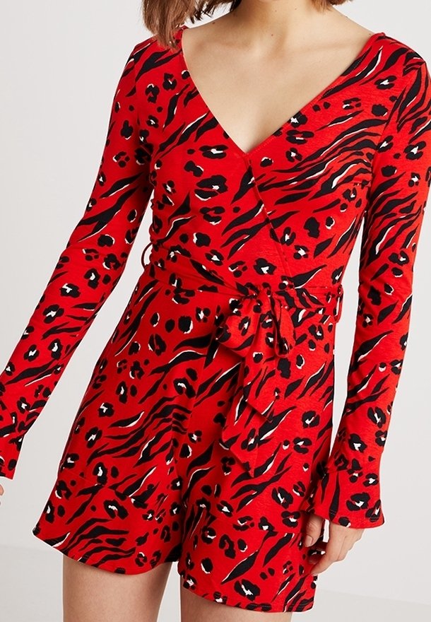 Femme portant une robe portefeuille rouge à imprimé animal noir et blanc avec des manches longues, nouée à la taille avec un nœud.