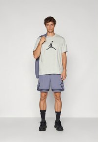 Grå bomulls t-skjorte med trykt logo, kombinert med lilla mesh-shorts med svarte striper. Sorte joggesko og sokker fullfører antrekket.