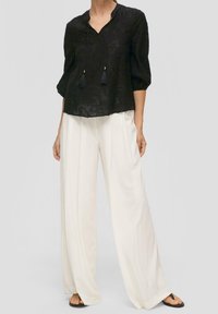 Blusa negra bordada con escote en V y lazos de borlas, combinada con pantalones anchos blancos que presentan una textura suave y un ajuste relajado.