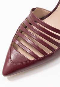 Ballerine in pelle bordeaux con punta appuntita e multiple aperture orizzontali sulla tomaia per la ventilazione. Interno foderato liscio.