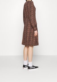 Abito leopardato marrone e nero, maniche lunghe, lunghezza al ginocchio, tessuto strutturato, abbinato a sneakers nere e calzini bianchi.