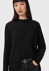 Maglione nero con un design diagonale testurizzato, maniche lunghe e scollo rotondo, abbinato a una cintura nera con una fibbia dorata.