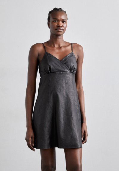 Rochie din piele neagră cu bretele subțiri reglabile, având un decolteu în formă de V și o croială lejeră, evidențiind o textură netedă și un design minimalist.