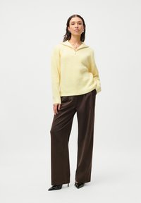 Light yellow ribbed sweater with a half-zip collar, paired with loose brown trousers and black pointed-toe heels; smooth textures.