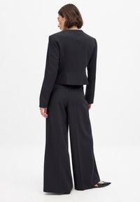 Black tailored jacket with a cropped design, paired with wide-leg trousers. Smooth fabric with minimalist lines and no visible fastenings.
