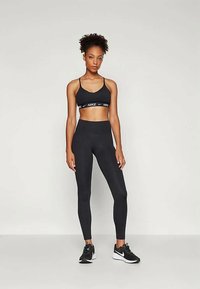 Svart sports-bh med en hvit Nike-logo og matchende høyt midje leggings, med en glatt, elastisk stoff og en tettsittende design. Svarte sneakers.