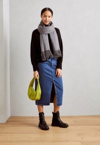 Pull en maille noire, jupe en denim bleu foncé avec fente, écharpe grise à franges, sac à main vert et bottines noires à glissières.