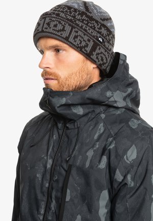 Black patterned jacket with a high collar, featuring a zipper and drawstrings. Dark gray knitted beanie with a geometric design.
