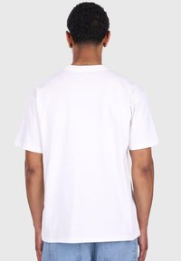 Hvid bomulds t-shirt med korte ærmer, rund halsudskæring og ensfarvet ryg. Ingen synlige mønstre eller grafik. Stoffet ser glat ud.