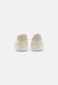 Beige joggesko med teksturert stoff og glatte detaljer. Har en hvit såle og en subtil logo ved hælen. Sikkert slip-on design.