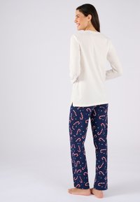 Helles cremefarbenes Langarmoberteil kombiniert mit dunkelblauen Hosen, die ein Zuckerstangenmuster in Rot und Weiß mit kleinen grünen Akzenten aufweisen.