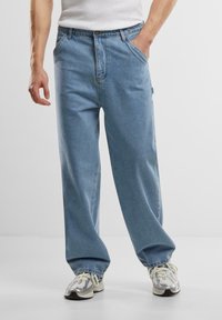 Lyseblå denimjeans med løs pasform, der har lynlås, forlommer og lige ben, parret med sølvfarvede træningssko.