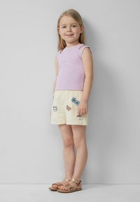 Lichtpaarse geribde tanktop en gele shorts met kleurrijke bloem- en dierenborduursels, gecombineerd met bruine sandalen met banden.
