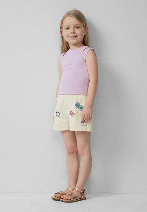 Lichtpaarse geribde tanktop en gele shorts met kleurrijke bloem- en dierenborduursels, gecombineerd met bruine sandalen met banden.