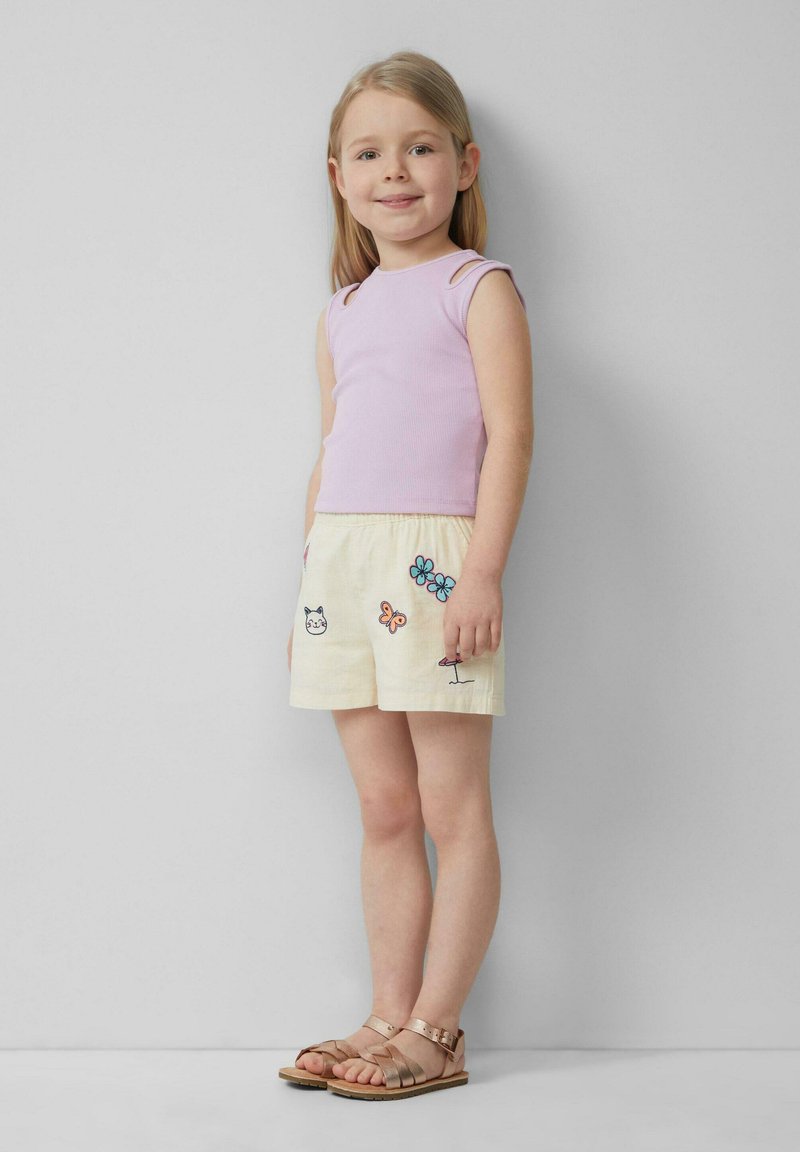 Lichtpaarse geribde tanktop en gele shorts met kleurrijke bloem- en dierenborduursels, gecombineerd met bruine sandalen met banden.