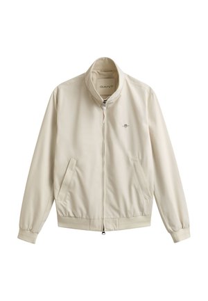 Beige Jacke mit Reißverschluss, Stehkragen, elastischen Bündchen und Saum, zwei Fronttaschen und kleinem, auf der Brust besticktem Logo.