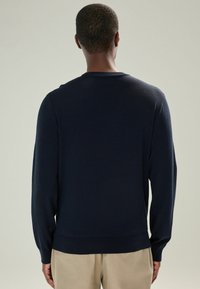 Pulover navy cu mâneci lungi, cu guler și tiv cu dungi. Textură moale, caracterizat printr-o siluetă ajustată și un finisaj curat.