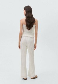 Lichtgewicht, gestructureerd crème ensemble met een gerimpeld, volante tube top en flaired broek met een diamanten patroon. Eenvoudige, gecoördineerde uitstraling.