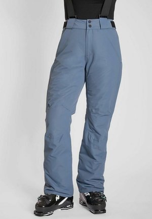 Blå isolerede skibukser med sorte seler båret med sorte skistøvler på hvid baggrund.