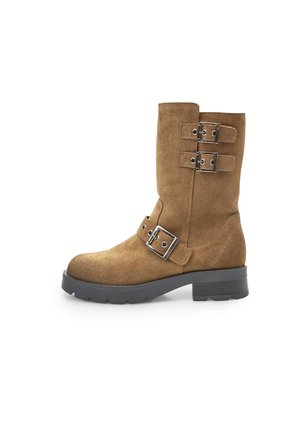 Stivale alla caviglia in suede marrone con punta arrotondata, due cinghie metalliche con fibbia e suola nera spessa. Dettaglio di cuciture verticali sulla parte superiore.
