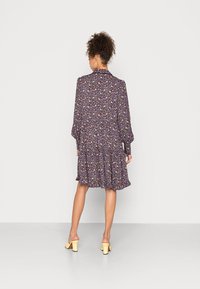 Vestido floral com mangas longas, bainha ondulada e um fundo escuro. Apresenta pequenas flores coloridas. Usado com sapatos de salto bloco amarelos.