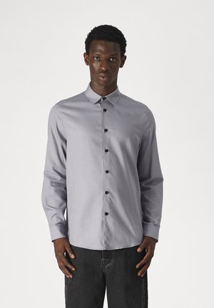 Grå langermet skjorte med knapper og krage, og svarte knapper. Stoffet ser glatt ut med en subtil glans.