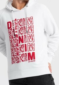 Bílá mikina s kapucí, která má na přední straně opakovaný text "DENIM" v tučném červeném písmu, se stahovacími šňůrkami a žebrovanými manžetami. Jemná tkanina s volným střihem.
