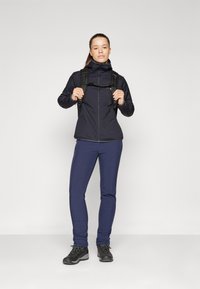 Juodas zip-up striukė, tamsiai mėlyni kelnės ir juodi žygio batai. Striukė turi aukštą apykaklę; apranga tinkama lauko veikloms.