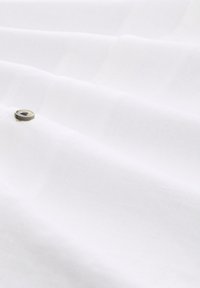 Weißer Stoff mit glatter Textur, versehen mit horizontalen Falten und einem metallischen Druckknopf-Detail.