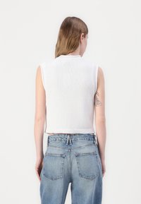 Hvit ermeløs strikket topp med en teksturert finish, rund hals og ribbestrikket kant. Båret med lyseblå høyt liv jeans.