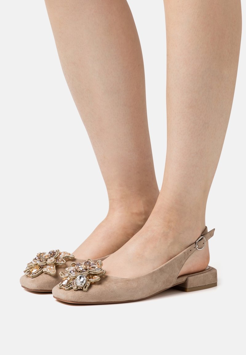 Voeten in beige suede slingback ballerina's met een lage hak en decoratieve beaded bloemversieringen op de tenen.