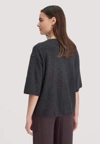 Maglia a maniche corte in grigio scuro, realizzata a maglia, con una vestibilità comoda, scollatura rotonda e orlo a coste, mostrata da dietro con una leggera trama.