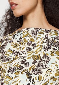 Top estampado con fondo crema, hojas verdes y manchas de leopardo negras. La tela tiene una textura suave y un escote relajado.