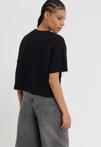 Black cropped t-shirt with short sleeves, paired with high-waisted, faded gray wide-leg jeans featuring back pockets and subtle stitching.