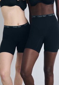 Mustad Calvin Kleini lühikesed püksid, millel on sile tekstuur ja elastne vöökoht, keha lähedane lõige, mis rõhutab kandjate kontrastseid nahatoonid.