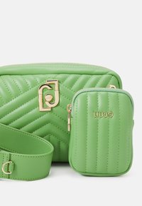 Groene gewatteerde synthetische schoudertas met gouden hardware en een afneembare kleine tas, met een chevronpatroon en een verstelbare schouderriem.