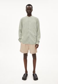 Lichtgroen overhemd met lange mouwen en een mandarinnekraag, gecombineerd met beige shorts en zwarte instapschoenen.