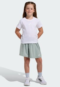 White short-sleeve t-shirt with a subtle three-stripe logo, paired with light green shorts featuring small texture details. White sneakers.