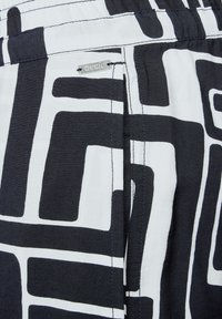 Svart och vitt mönstrat tyg med stora abstrakta former. Har en sydd etikett märkt "CECIL." Slät textur, elastisk midja.