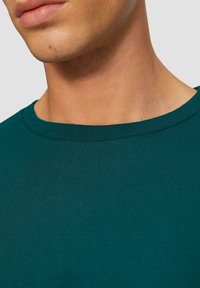 Teal katoenen t-shirt met een ronde hals, voorzien van een zachte textuur en een close-up van de stof langs de kraag en nekgebied.