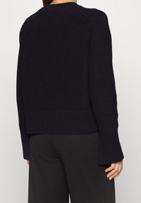 Pull tricoté bleu marine avec ourlet et poignets côtelés, présentant un motif texturé et une coupe légèrement courte. Design minimaliste sans ornements.
