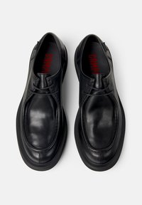Ein Paar schwarze Leder Schnürschuhe mit abgerundeten Zehen und dicken Sohlen, von oben auf einem weißen Hintergrund betrachtet.