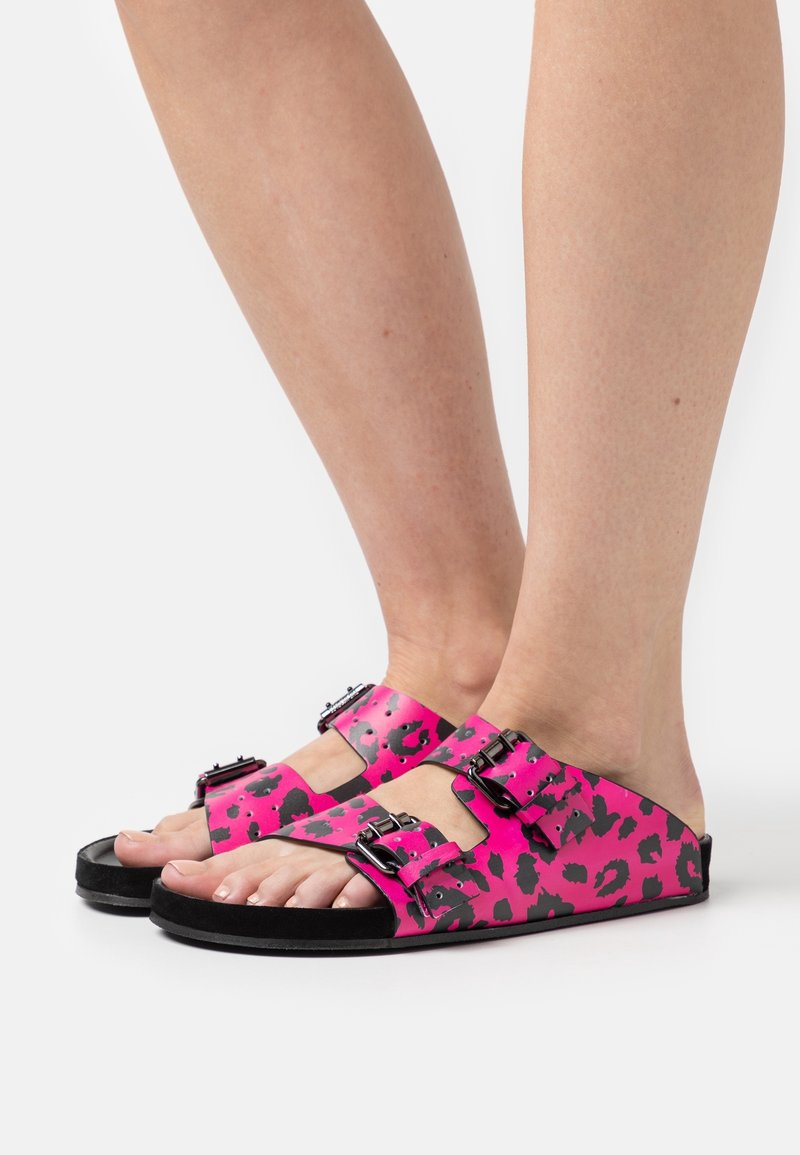 Rosa leopardmönstrade sandaler med svarta detaljer, två justerbara remmar och en platt sula. Materialet verkar vara syntetiskt med en slät textur.