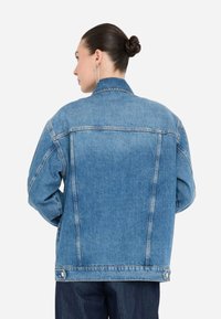 Giubbotto di jeans di un blu chiaro con colletto, vestibilità comoda e due cuciture posteriori. Presenta tasche frontali e chiusura con bottone all'orlo.