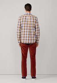 Camisa de cuadros en azul, naranja y amarillo, con cuello abotonado y mangas largas; combinada con pantalones de pana en color óxido y zapatos oscuros.